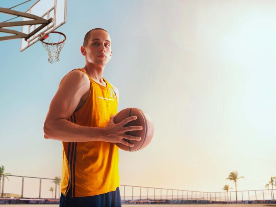 Tall basketball player holding a ball on an outdoor court at sunset